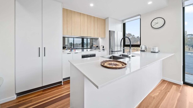 A modern kitchen with white cabinetry, a large island, stainless steel appliances, and a view through the window. - Inner-City 2-Bed with Large Balcony, Garden & Gym (Campbell)