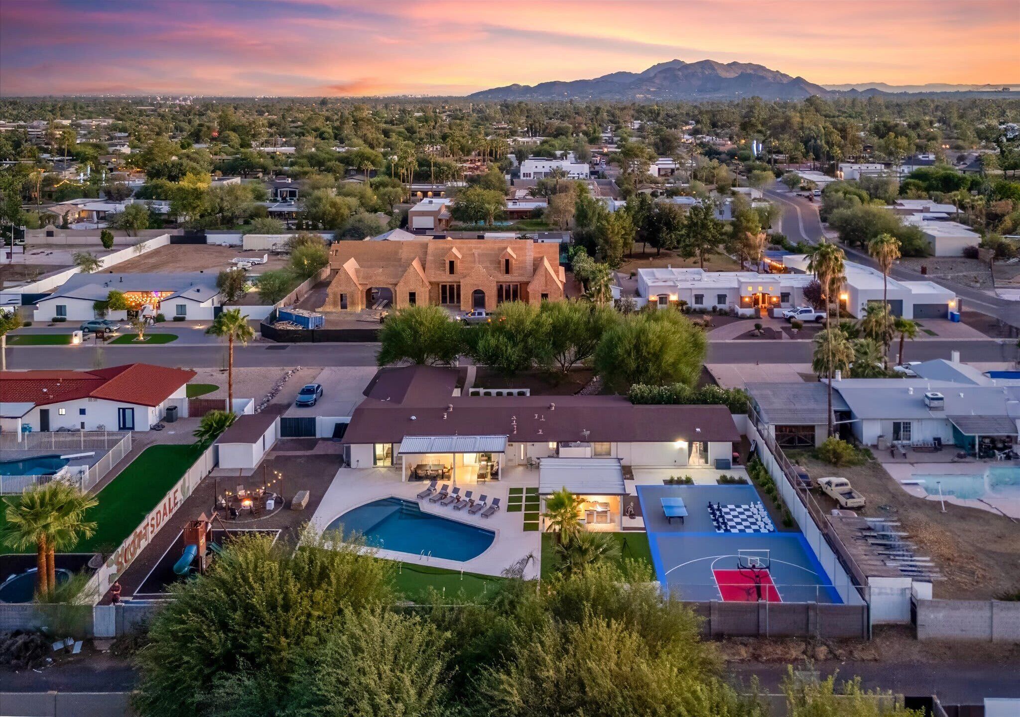 Zona residencial amb una casa gran que té una piscina, una pista de bàsquet i un jardí ben cuidat.