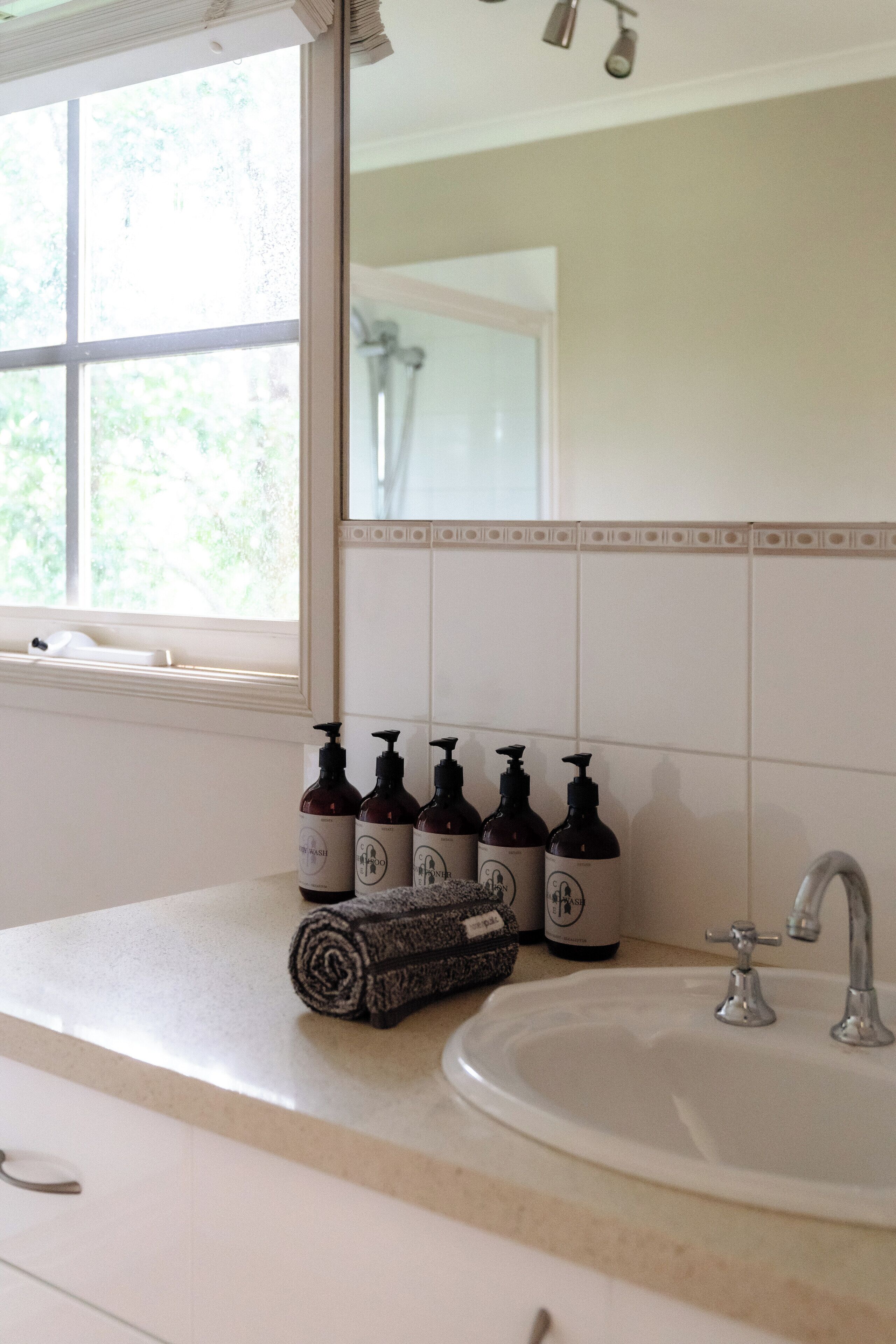 A bathroom with a sink, a mirror, and a window. There are bottles of shampoo and conditioner on the counter.