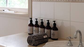 A bathroom with a sink, a mirror, and a window. There are bottles of shampoo and conditioner on the counter.