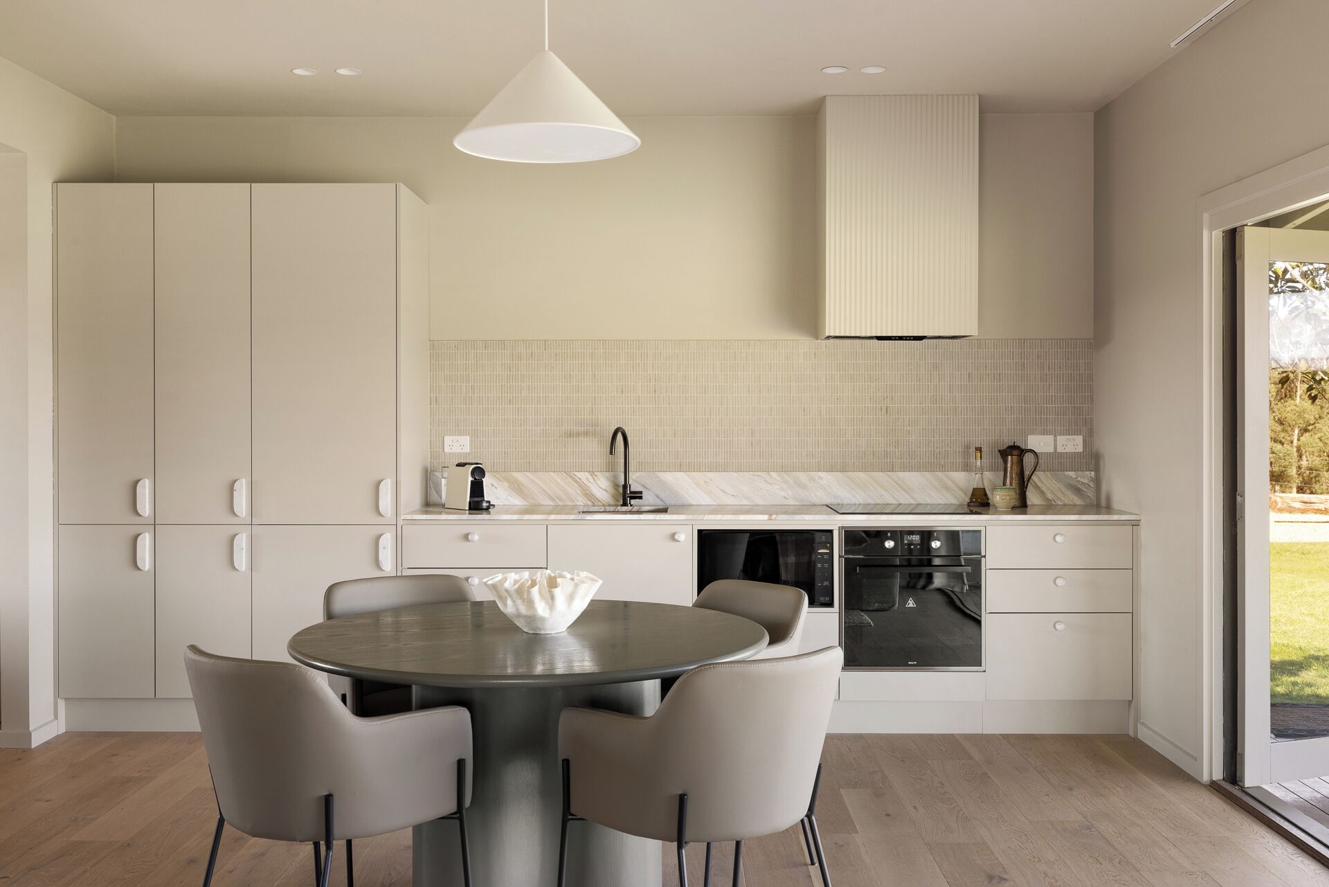 A modern kitchen with a round dining table, built-in appliances, and a view to the outdoors.