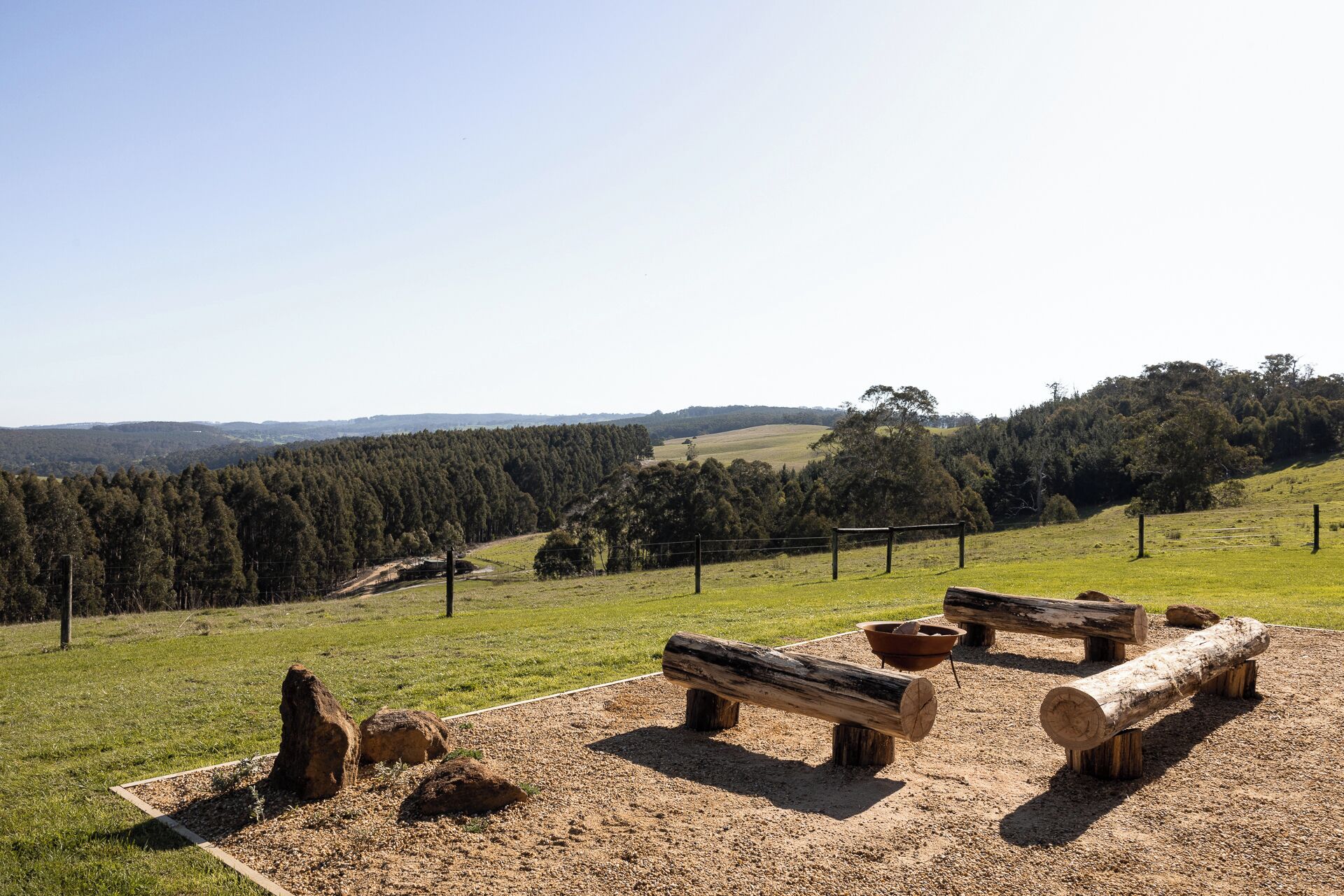 Un espace extérieur agréable, avec un sentier de terre, des bancs en bois et une vue sur une colline boisée.