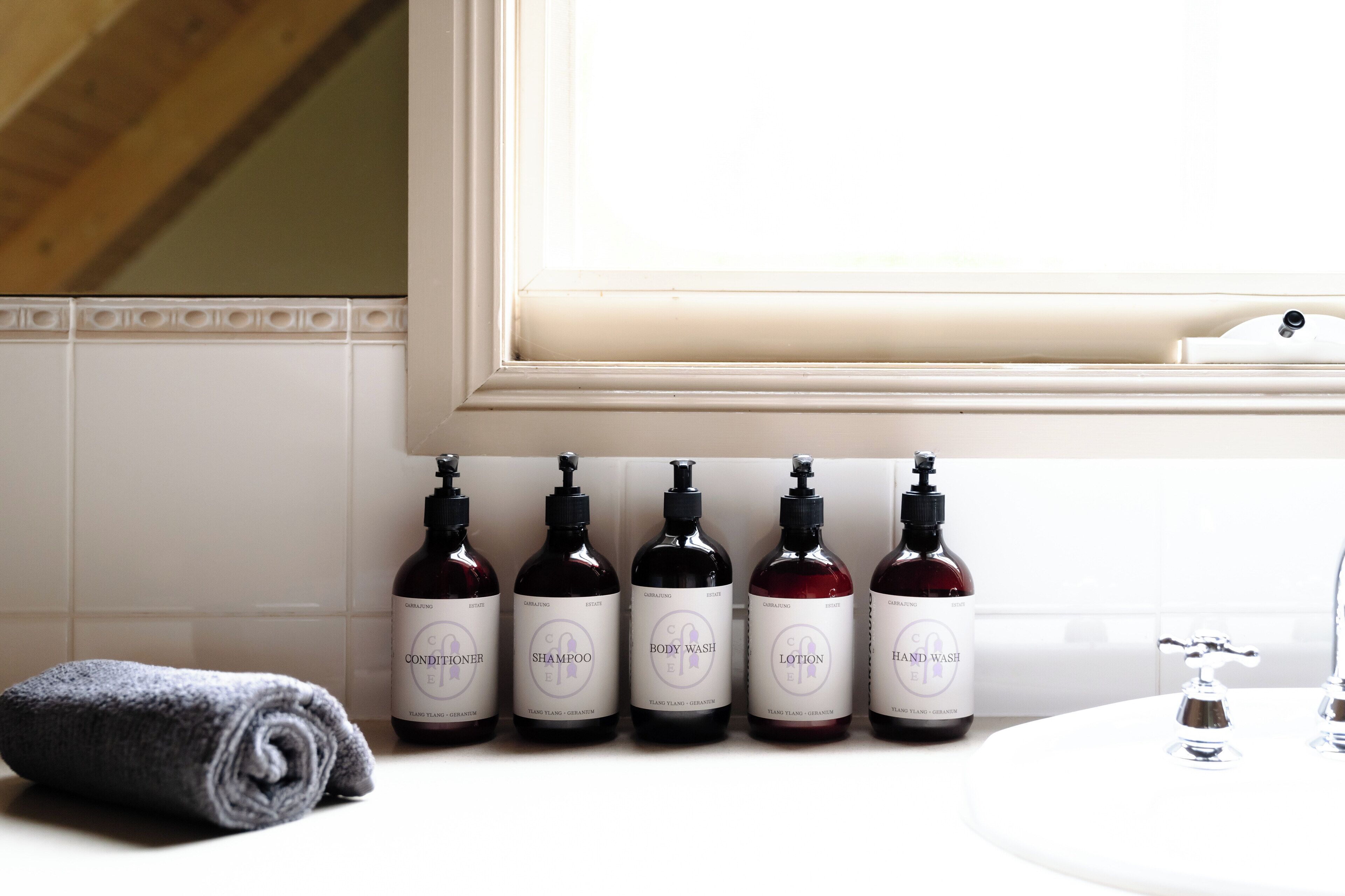 A bathroom with a white sink, a towel, and five bottles of shampoo, body wash, lotion, and hand wash.