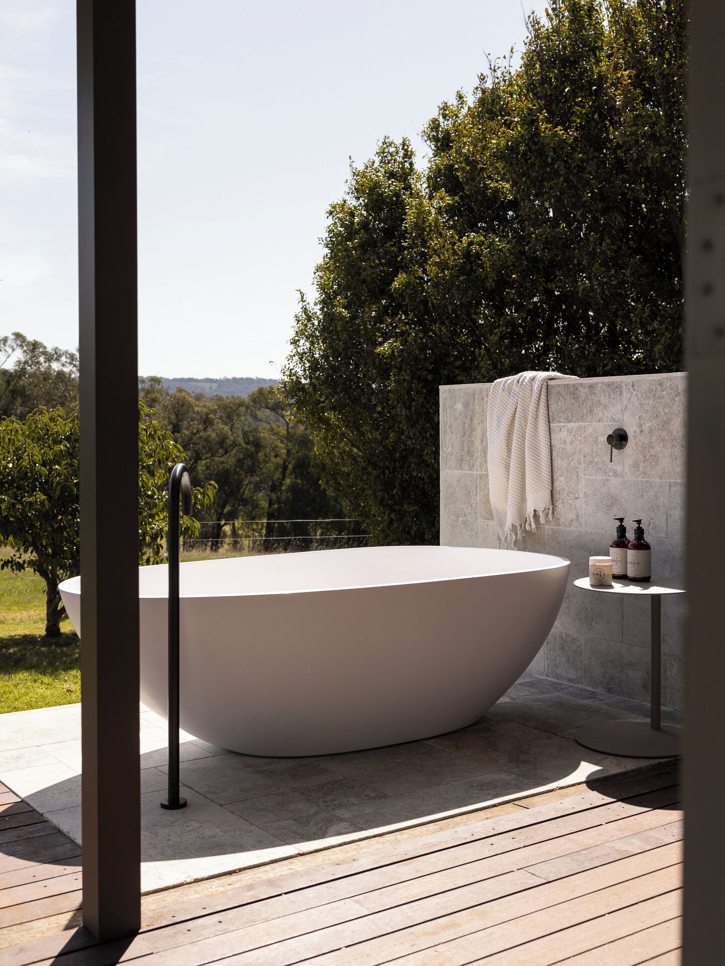 Una bañera moderna al aire libre con vista a un jardín exuberante y colinas.