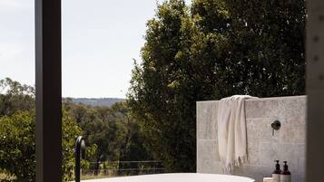Una bañera moderna al aire libre con vista a un jardín exuberante y colinas.
