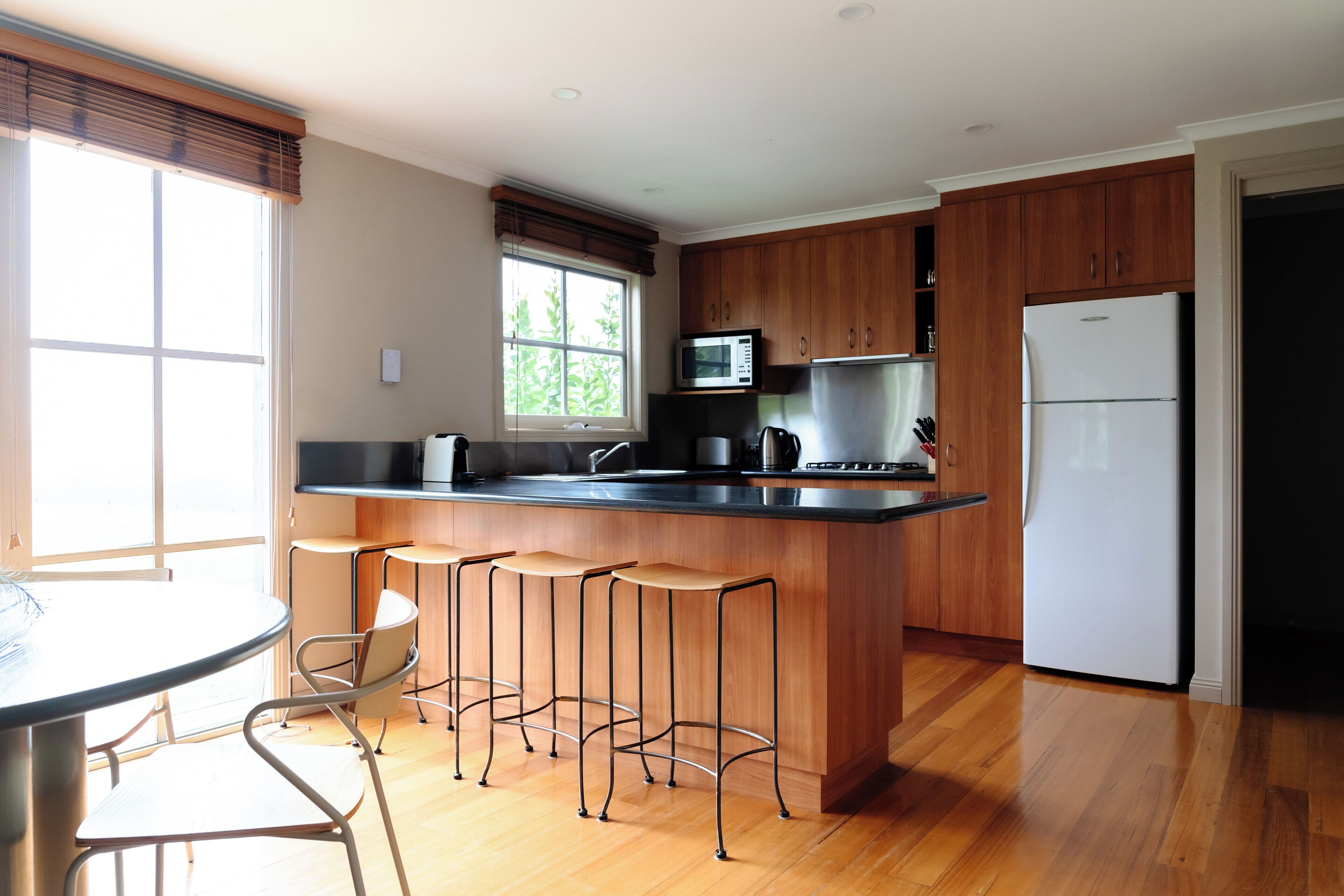 Une cuisine moderne avec des meubles en bois, un réfrigérateur en acier inoxydable, un four à micro-ondes et un coin bar avec des tabourets.