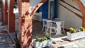 Un espace extérieur abrité, aménagé avec une table et des chaises, entouré d’arches en briques et de plantes en pot.