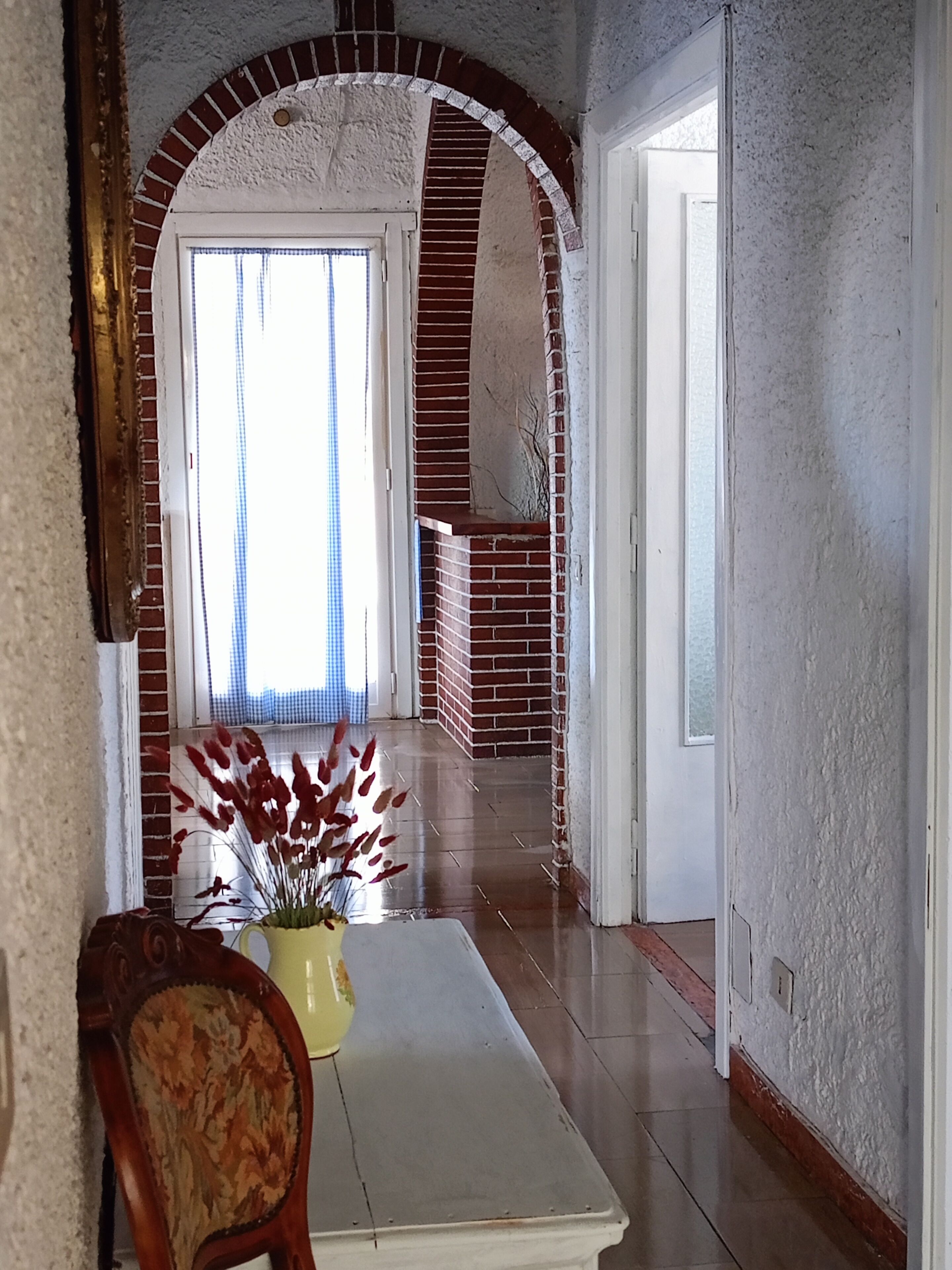 A hallway with a white door, a brick fireplace, and a yellow vase with red flowers on a white table.