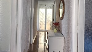 Un couloir aux murs blancs et au plancher en bois, qui mène à une porte dotée d’un panneau en verre dépoli.