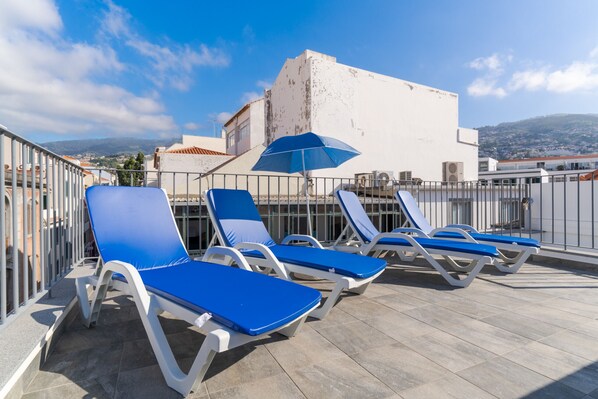 Une terrasse sur le toit avec plusieurs fauteuils bleus et un parasol bleu.