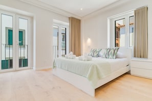 A modern bedroom with a large bed, a bedside table, a wardrobe, and a window with curtains.