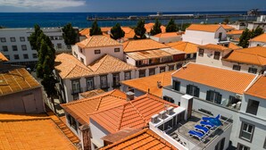 A coastal town with terracotta-roofed buildings, a marina, and a clear blue sky.