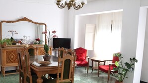 A dining area with a wooden table and chairs, a television, and a red armchair.