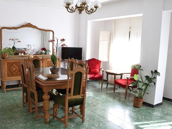 A dining area with a wooden table and chairs, a television, and a red armchair.