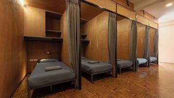 A room with four beds arranged in a row, wooden walls, and a herringbone floor pattern.