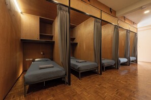 Egy szoba, amelyben négy ágy egymás mellett, sorban van elrendezve, a falak fából vannak, és a padló heringminta szerint van lerakva.