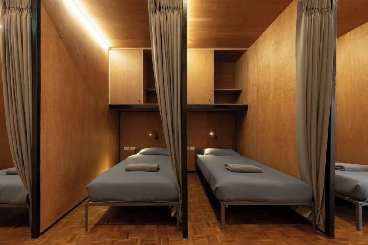 A room with four single beds, wooden walls, and a herringbone floor pattern.