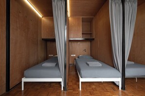 Una habitación con dos camas individuales, suelo de madera y una estantería empotrada.
