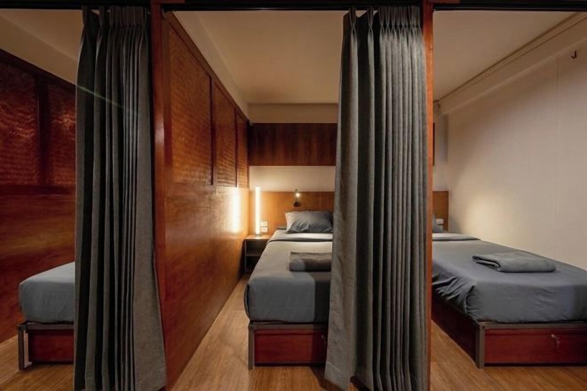 A hotel room with two beds, a wooden wardrobe, and a nightstand with a lamp.