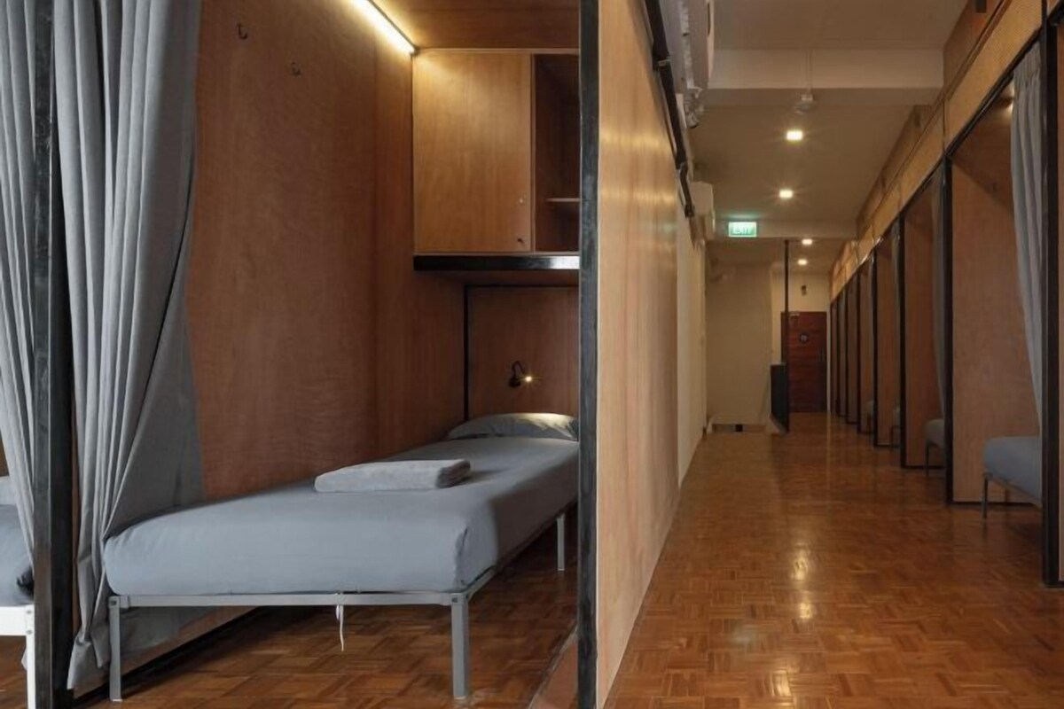 A narrow hallway with a bed on the left and a row of chairs on the right.