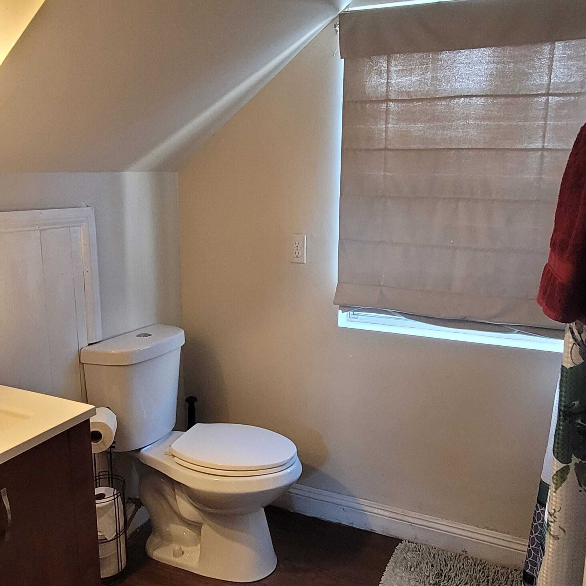 Un baño pequeño y funcional con inodoro, lavamanos y ventana con persiana.