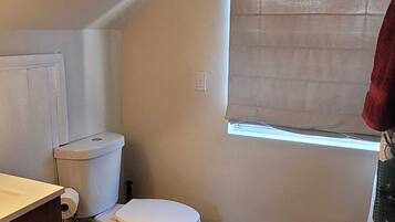 Un baño pequeño y funcional con inodoro, lavamanos y ventana con persiana.