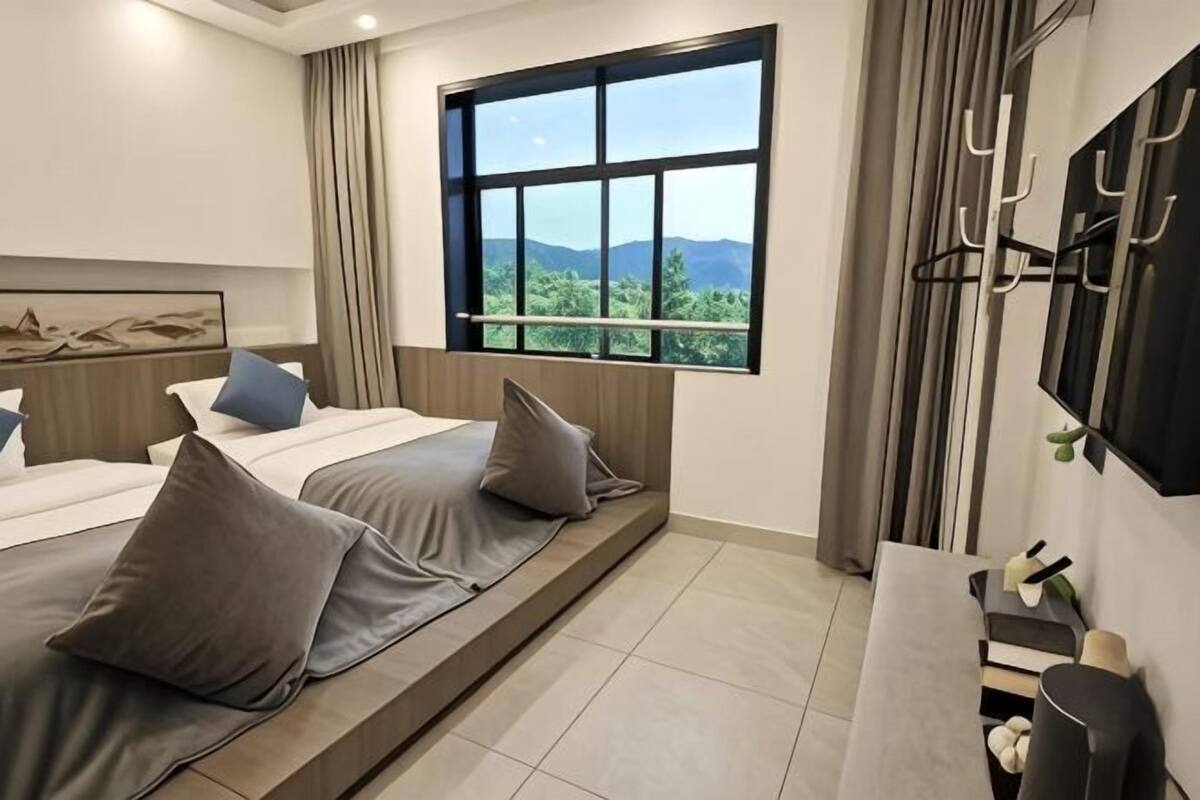 Habitación de hotel con un ventanal grande, una cama con almohadas, una mesita de noche y un televisor montado.
