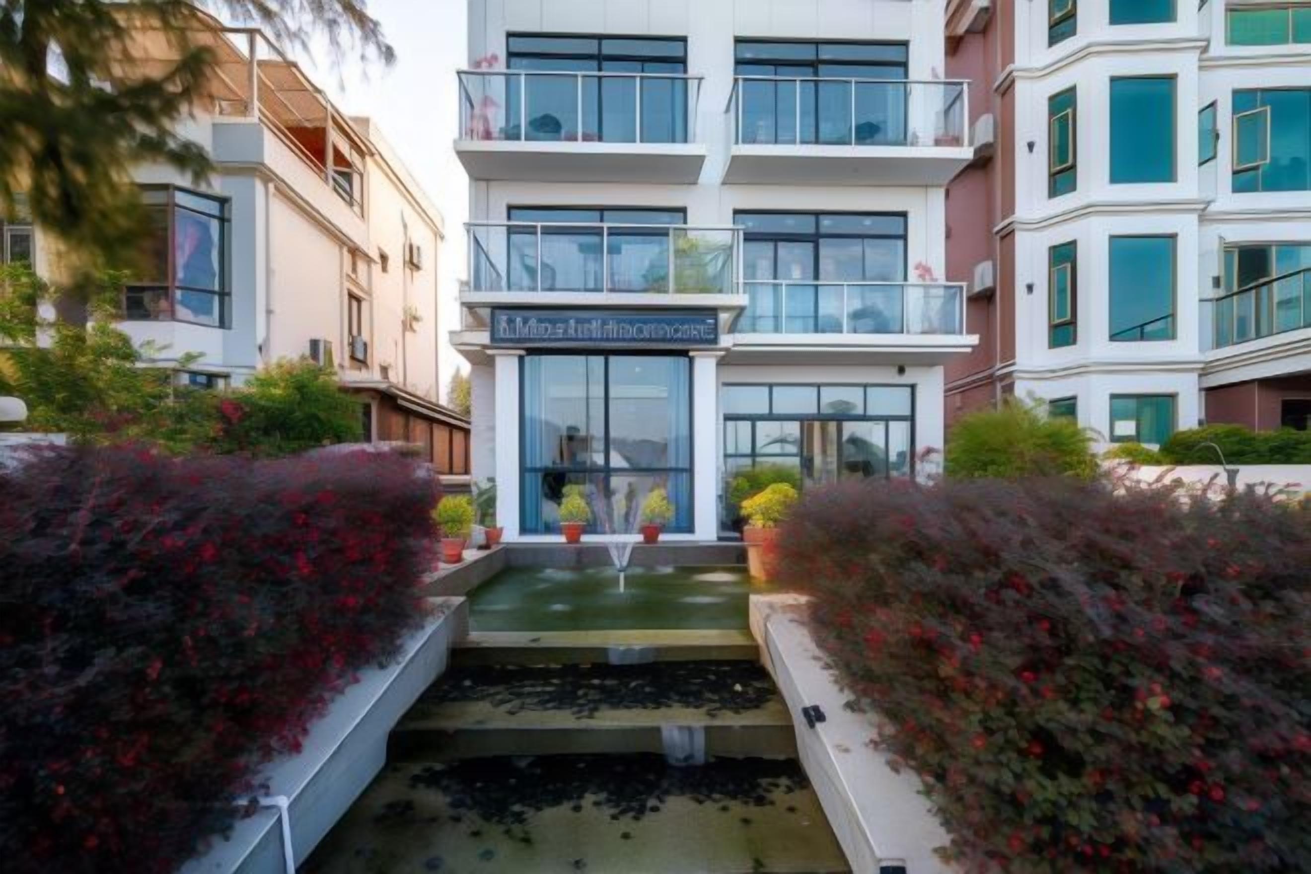 Un hotel con fachada moderna, entrada central y un pequeño elemento decorativo de agua en el patio.
