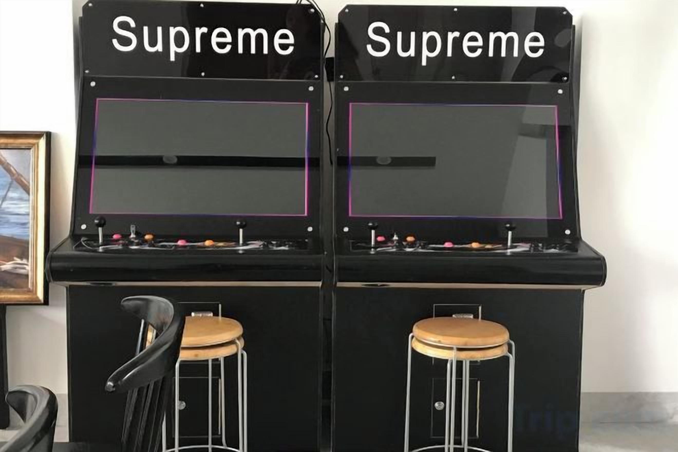 Dos máquinas de arcade llamadas 'Supreme' con paneles de control y taburetes.