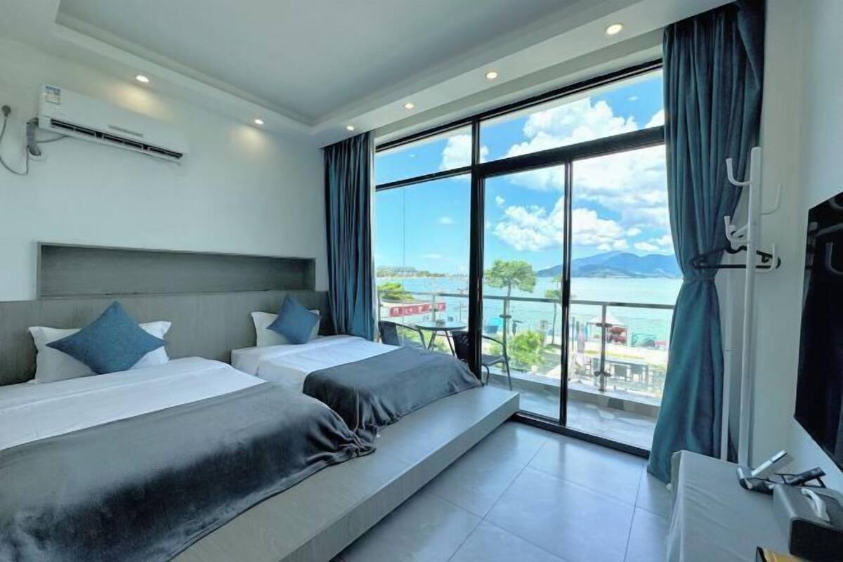 Una habitación de hotel moderna con dos camas, un ventanal con vistas al mar y un aire acondicionado en la pared.