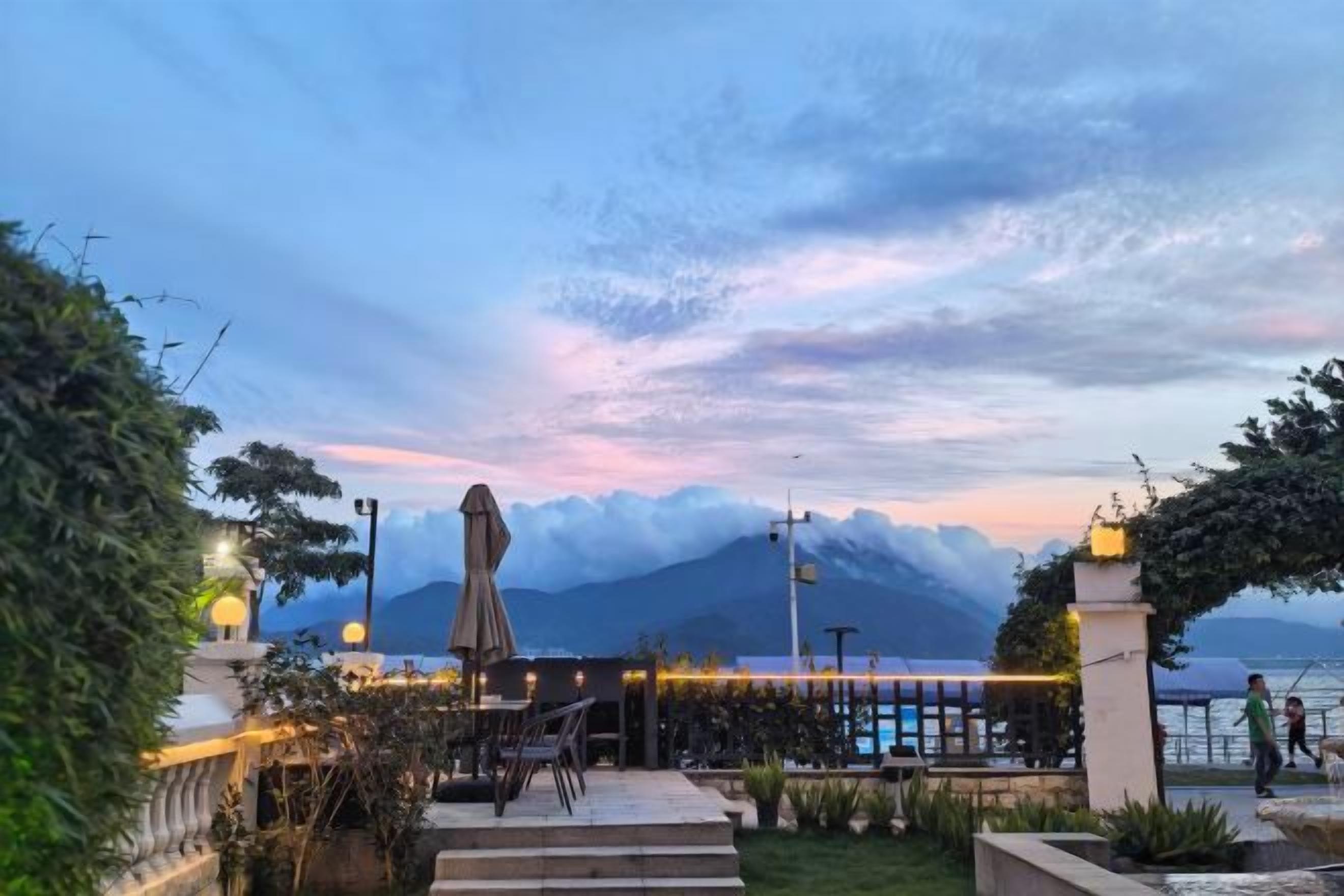 Un restaurante frente al mar con terraza, vistas al océano y una montaña al fondo.