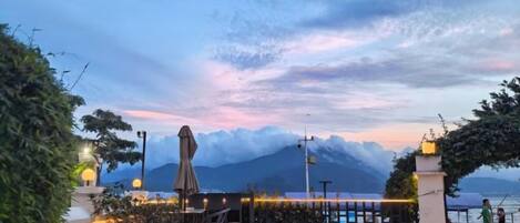 A waterfront restaurant with outdoor seating, a view of the sea, and a mountain in the background.
