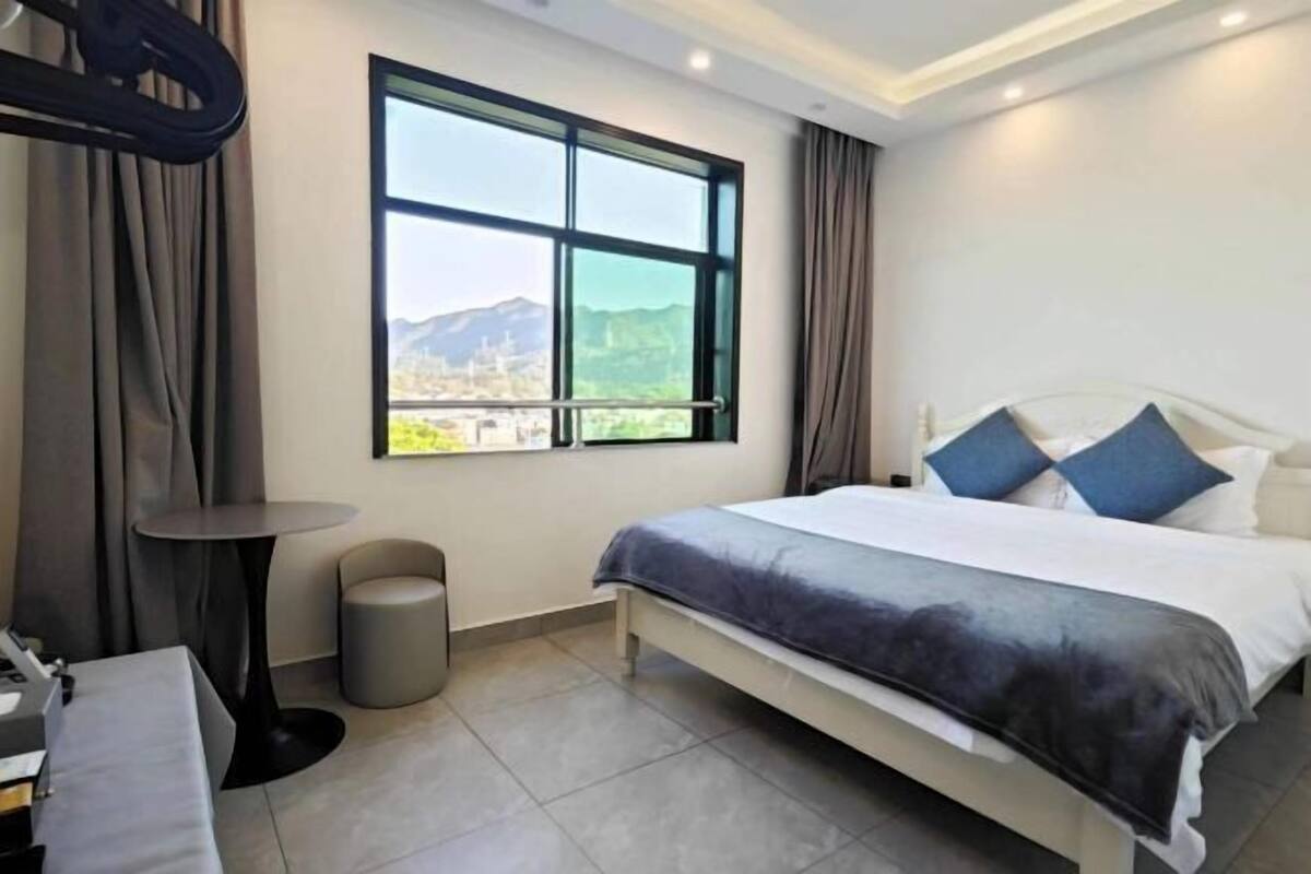 Habitación de hotel con cama, una mesita redonda, una silla, una ventana con vistas a montañas y una cortina.