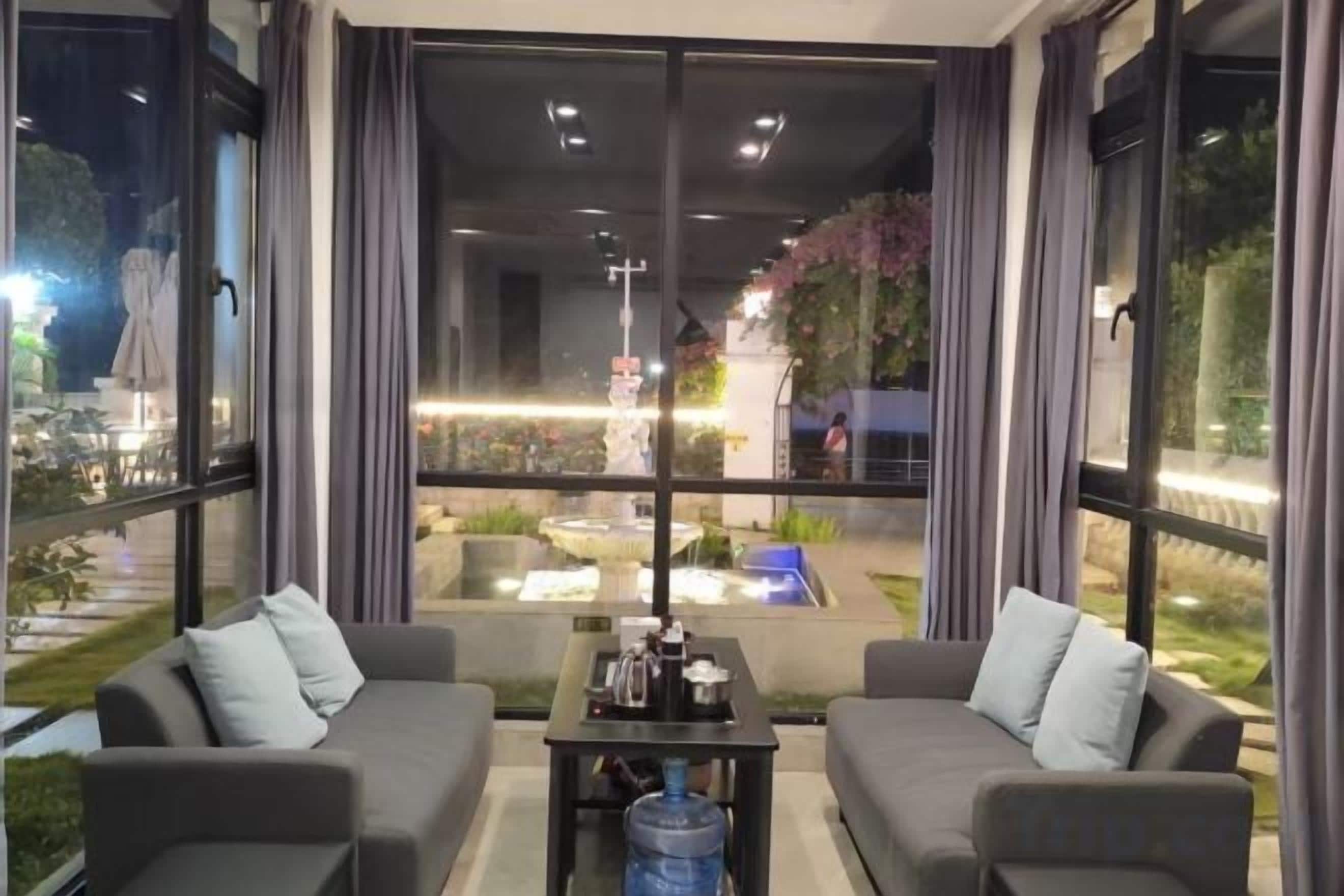 A modern room with two sofas, a coffee table, and large windows offering a view of an outdoor area with a fountain and greenery.