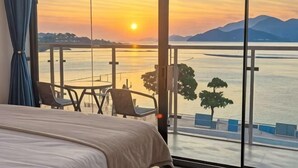 A room with a bed, a view of a sunset over water, and a balcony with chairs. - West Lafayette seaview Inn (Shenzhen)