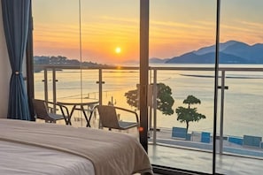 A room with a bed, a view of a sunset over water, and a balcony with chairs. - West Lafayette seaview Inn (Shenzhen)