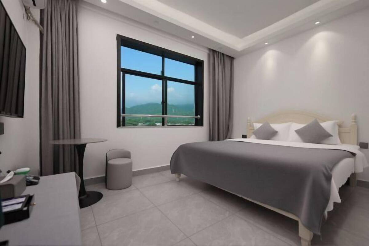 Habitación de hotel moderna con una cama grande, un escritorio, una silla, una mesita, una lámpara y una ventana con vistas.