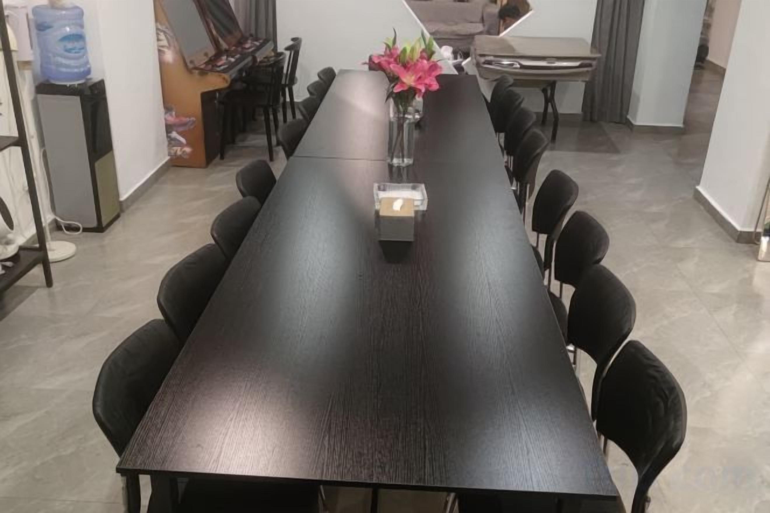 Una larga mesa de conferencias de madera oscura con sillas a su alrededor, un jarrón con flores y una pequeña caja sobre la mesa.