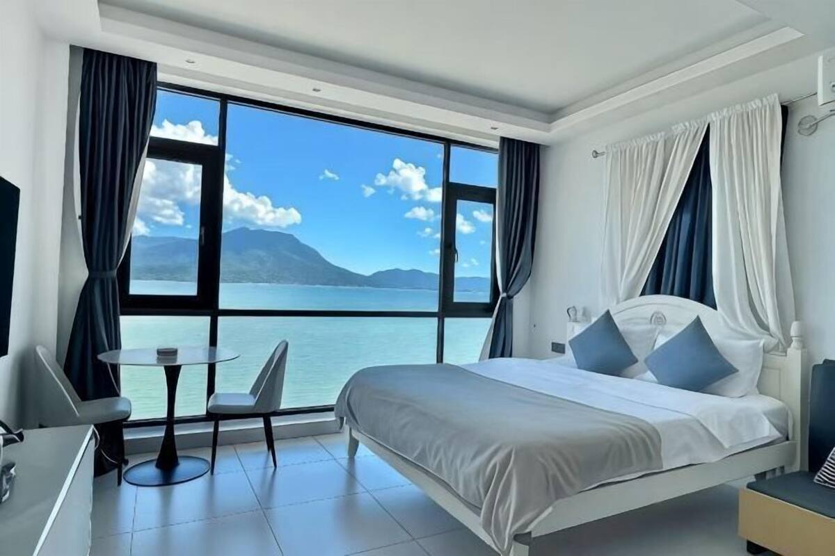Habitación de hotel con una cama grande, un escritorio con una silla, una mesita y vistas al mar.