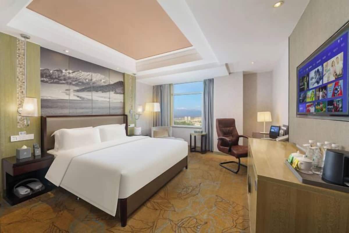 Une chambre d’hôtel avec un grand lit, un bureau équipé d’un ordinateur, une chaise et une vue sur la ville.
