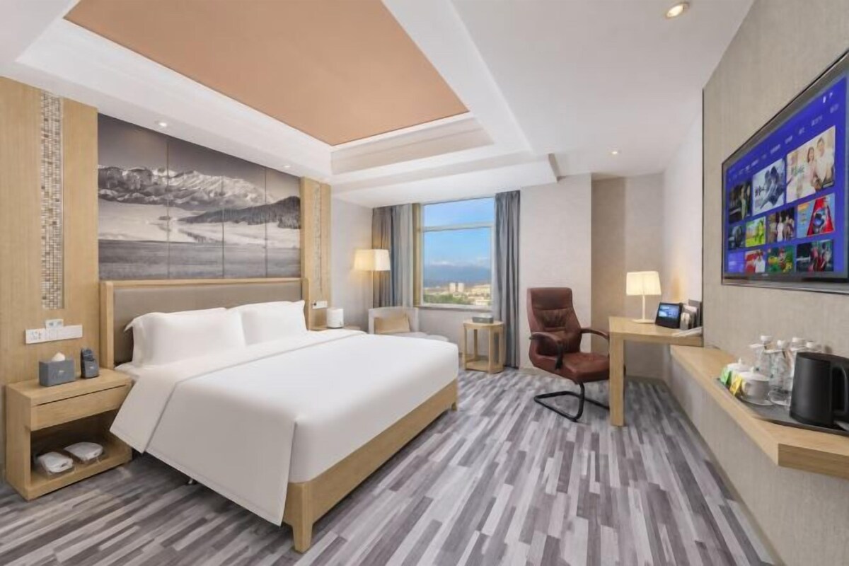 Quarto de hotel com uma cama grande, uma escrivaninha com cadeira, televisão e vista para a cidade.