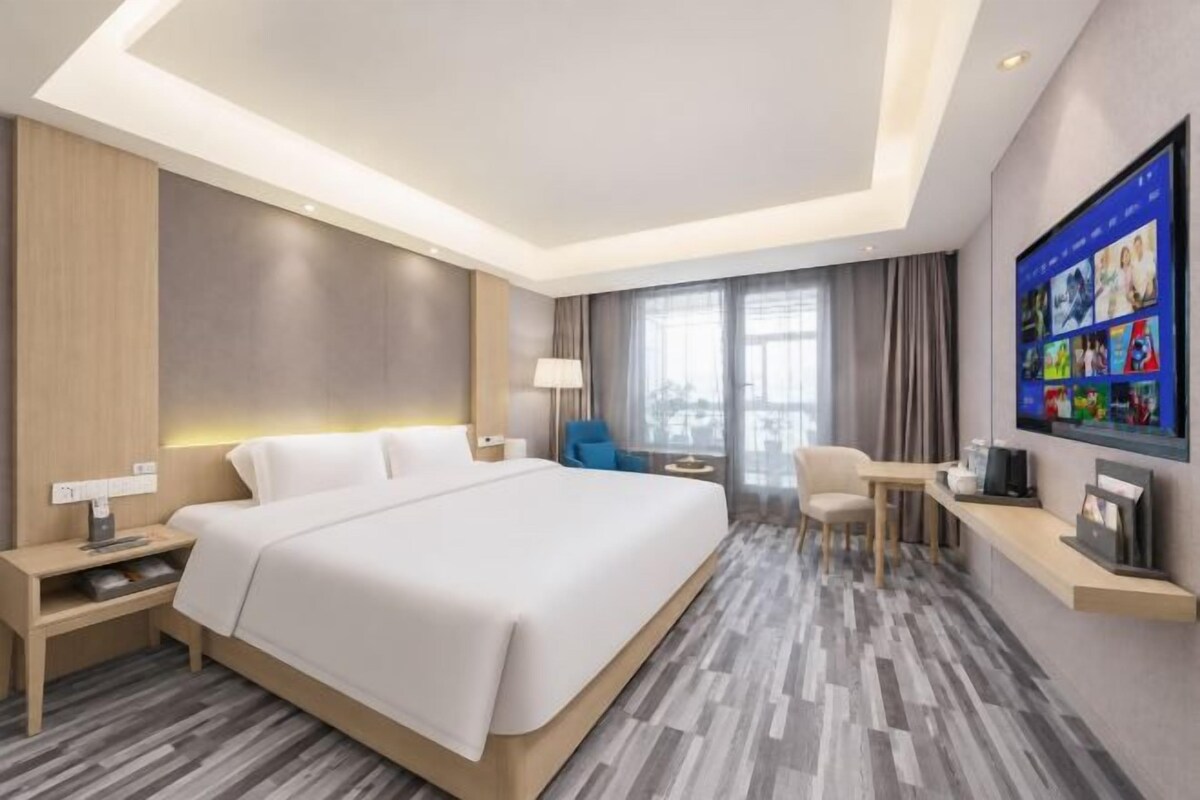 Quarto de hotel moderno com cama grande, mesas de cabeceira, escrivaninha e televisão.