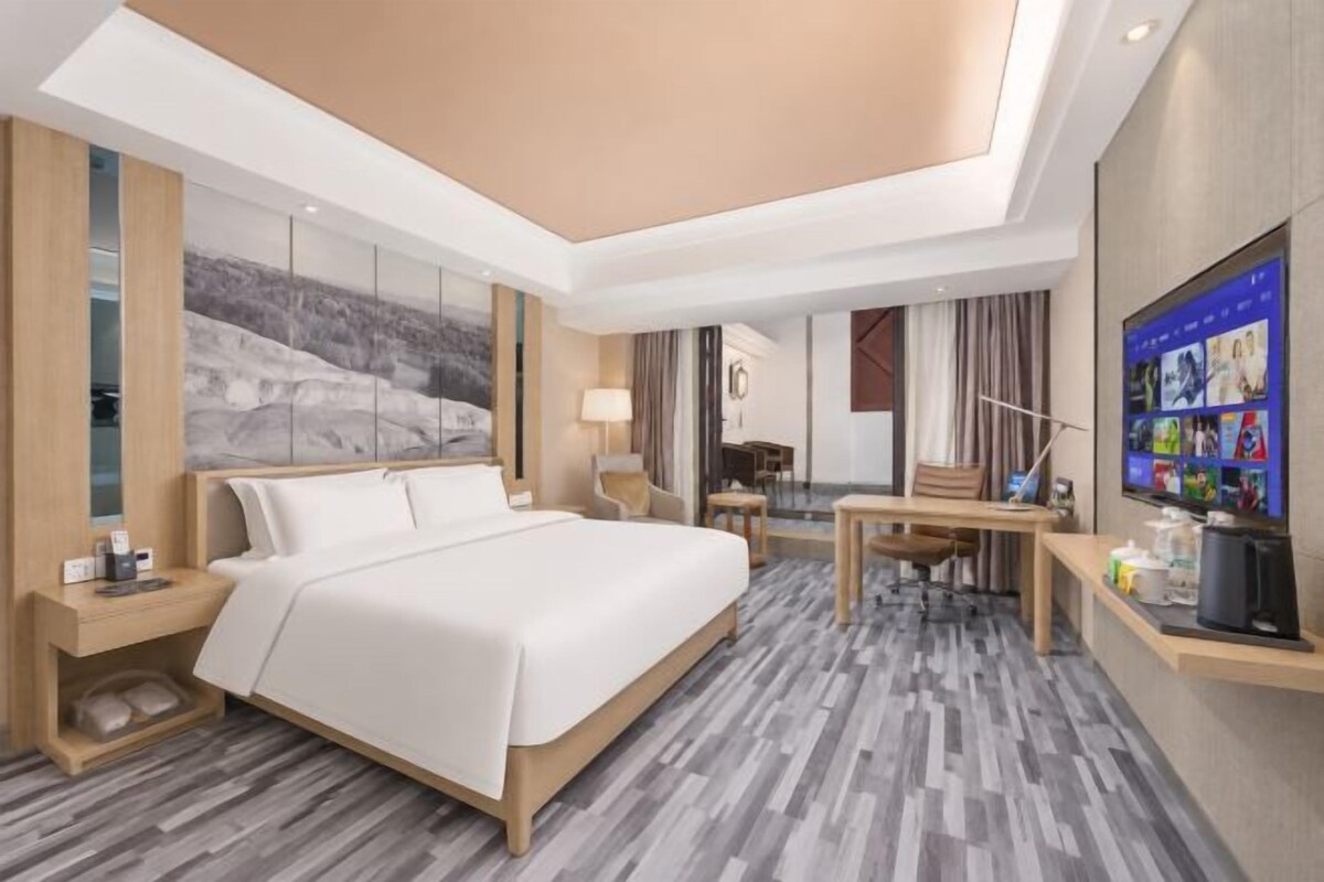 A modern hotel room with a large bed, a desk, a television, and a view of the outdoors.