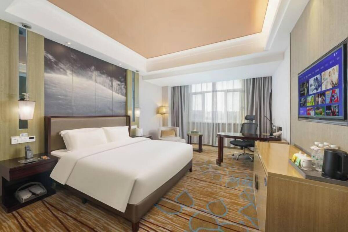 Une chambre d’hôtel avec un grand lit, un bureau, une chaise, une télévision et une fenêtre avec des rideaux.
