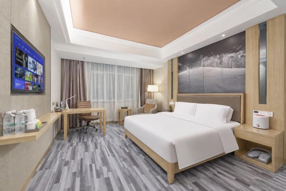 A hotel room with a bed, desk, chair, and a TV on the wall.
