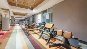 A gym with exercise equipment, a long mirrored wall, and a wooden ceiling. - Benison VII Boutique Hotel (Urumqi)