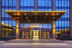 Ein moderner Hotel Eingangsbereich mit einer Drehtür, großen Fenstern und einem überdachten Vorbereich.