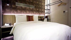 Quarto de hotel com uma cama grande, mesa de cabeceira com telefone, escrivaninha com cadeira e luminária pendente.