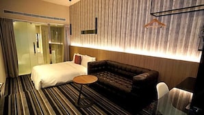 Quarto de hotel com uma cama, um sofá, uma mesinha redonda e um espelho.