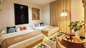 Quarto de hotel com duas camas, um quadro na parede, uma luminária e um vaso com planta.